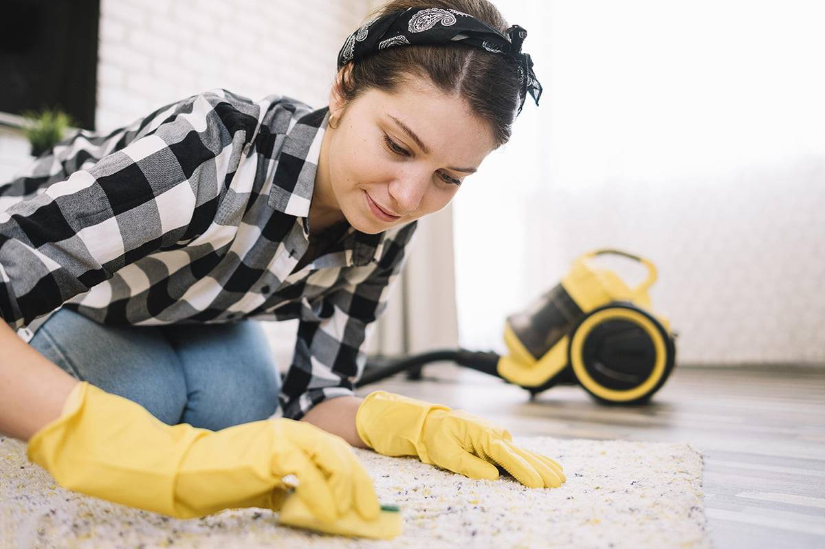 Young woman with checkered shirt cleaning a carpet rug