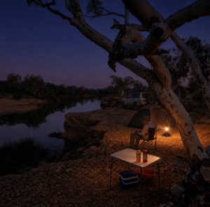 DIGGERS™ Citronella Torch and Lamp Oil bottles on a camp table beside a glowing lantern at an Australian bush campsite at dusk